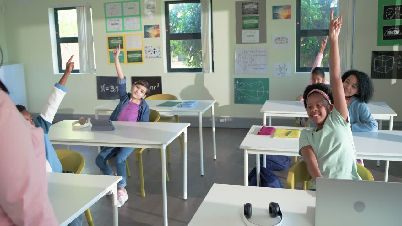 Pembe blazer giyen bir öğretmenin dizüstü bilgisayarla sınıfta sorduğu soruya ellerini kaldırarak cevap veren çeşitli genç öğrenciler