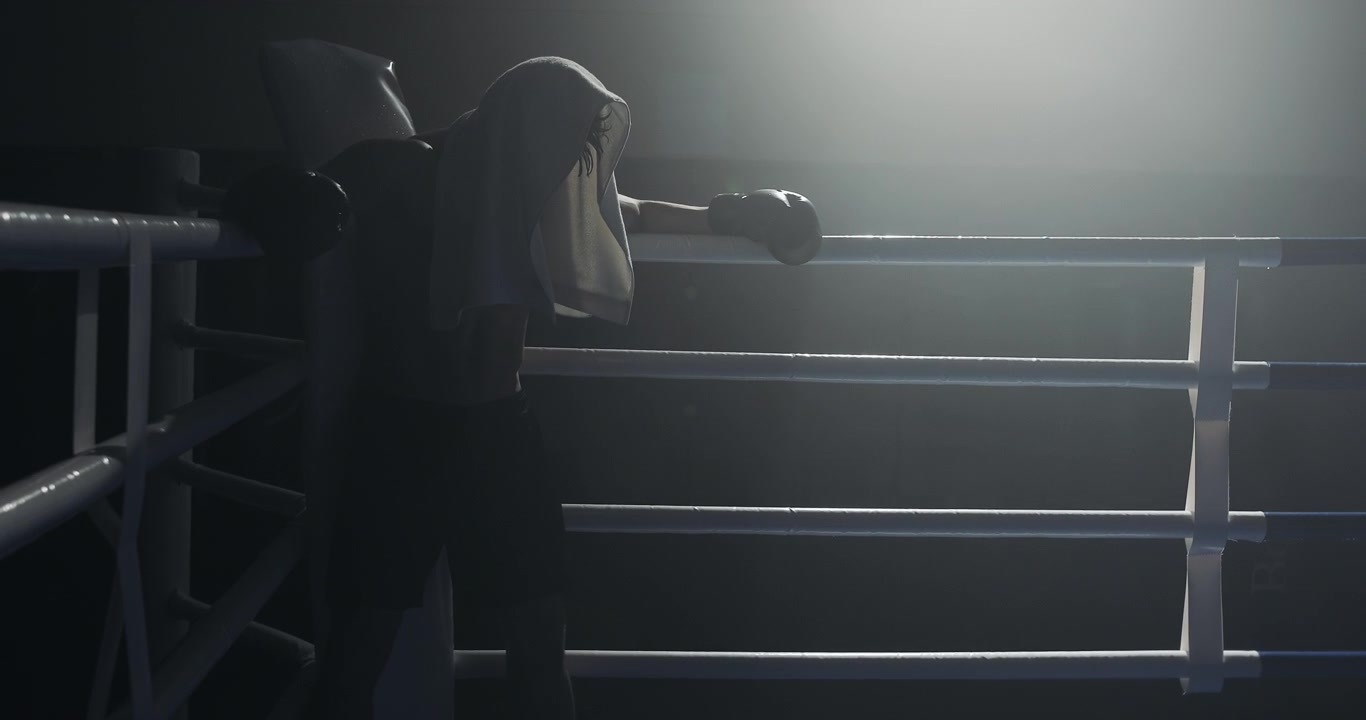 Silhouette drammatica di un pugile che riposa in un ring buio.