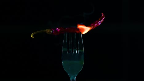 hot red chili pepper on a fork in flames on a black background