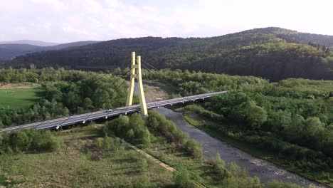 Enorme-Puente-Amarillo-En-El-Bosque,-Camiones-En-Movimiento-Y-Río-Que-Fluye---Toma-Aérea