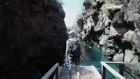 male with backpack walking towards edge of platform to view swimming pool at las grietas canyon in the galapagos