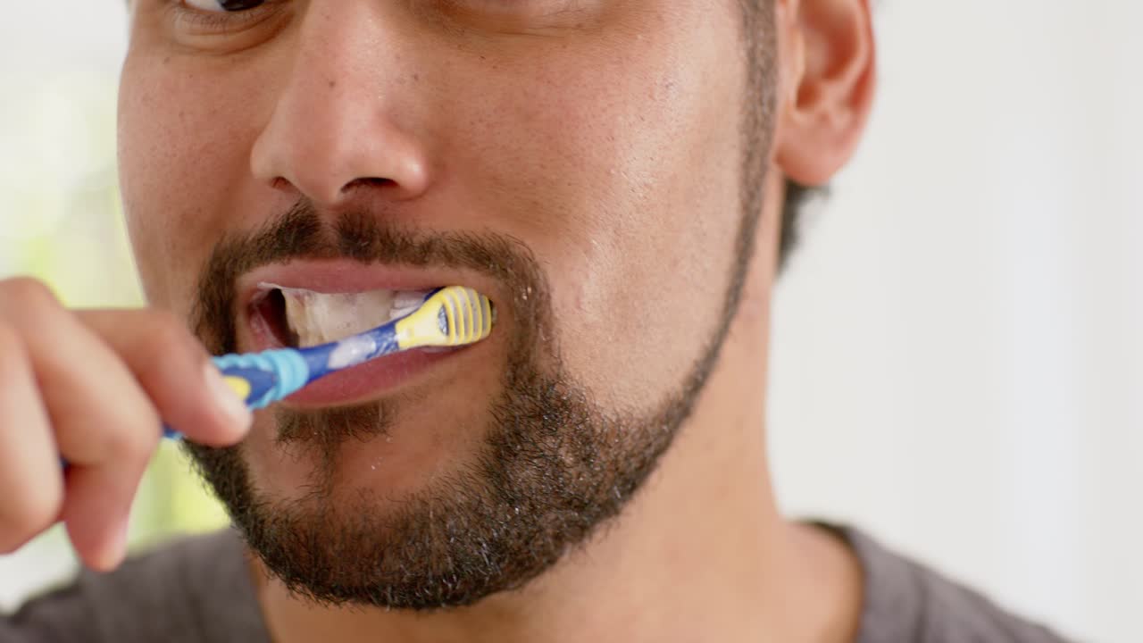 African American man brushing teeth with brush from left, producing white foam to clean in bathroom