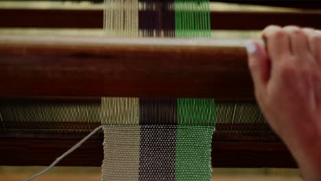 Top-down-view-of-skilled-woman-working-at-weaving-loom,-moves-shuttle-through-yarn