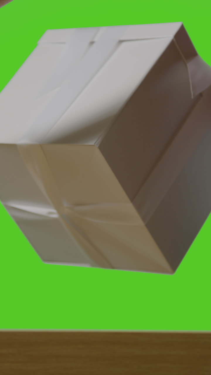 video vertical de un hombre poniendo un regalo en una caja envuelta en regalo decorada con cinta en una bolsa de regalo en la mesa disparado contra la pantalla verde 1