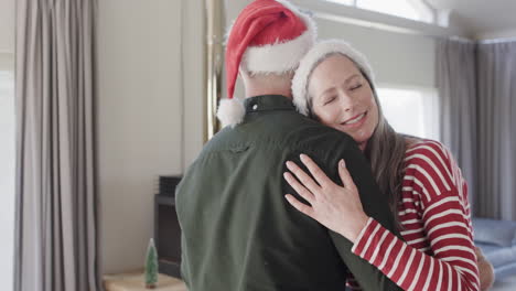 middle aged caucasian couple in santa hats dancing at christmas at home, slow motion