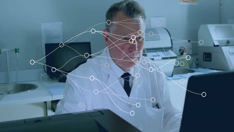 Senior male doctor working at laptop in medical lab, showing data flow overlay graphics