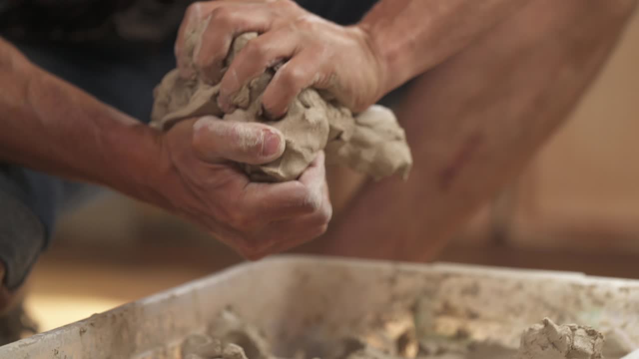 un primer plano de un alfarero amassando arcilla antes de moldear. un escultor masculino está tomando y dando forma a la arcilla para crear cerámica en su estudio
