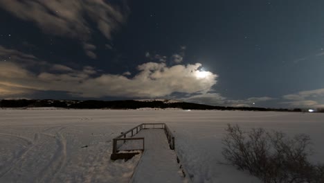 stable timelapse at 25 frames per second shows a frozen lake with people skying on top of it. moonlit shot with clouds moving infront of stars