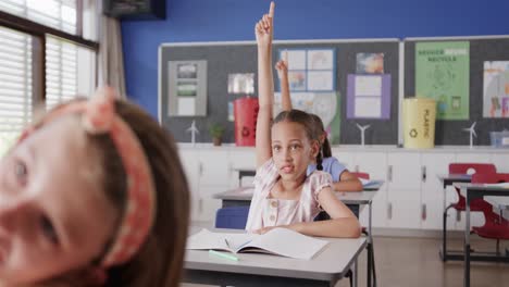 Colegialas-Felices-Y-Diversas-Levantando-La-Mano-En-Los-Escritorios-De-La-Clase-De-Escuela-Primaria,-Cámara-Lenta