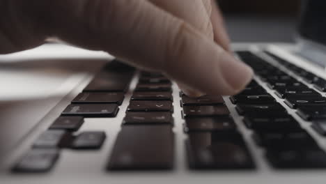 low-angle close-up of caucasian fingers typing on laptop keyboard