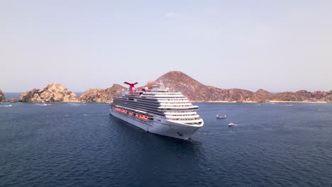 Un-Drone-Rodea-El-Crucero-Panorámico-Del-Carnaval-Anclado-En-La-Bahía-De-Cabo-San-Lucas,-México