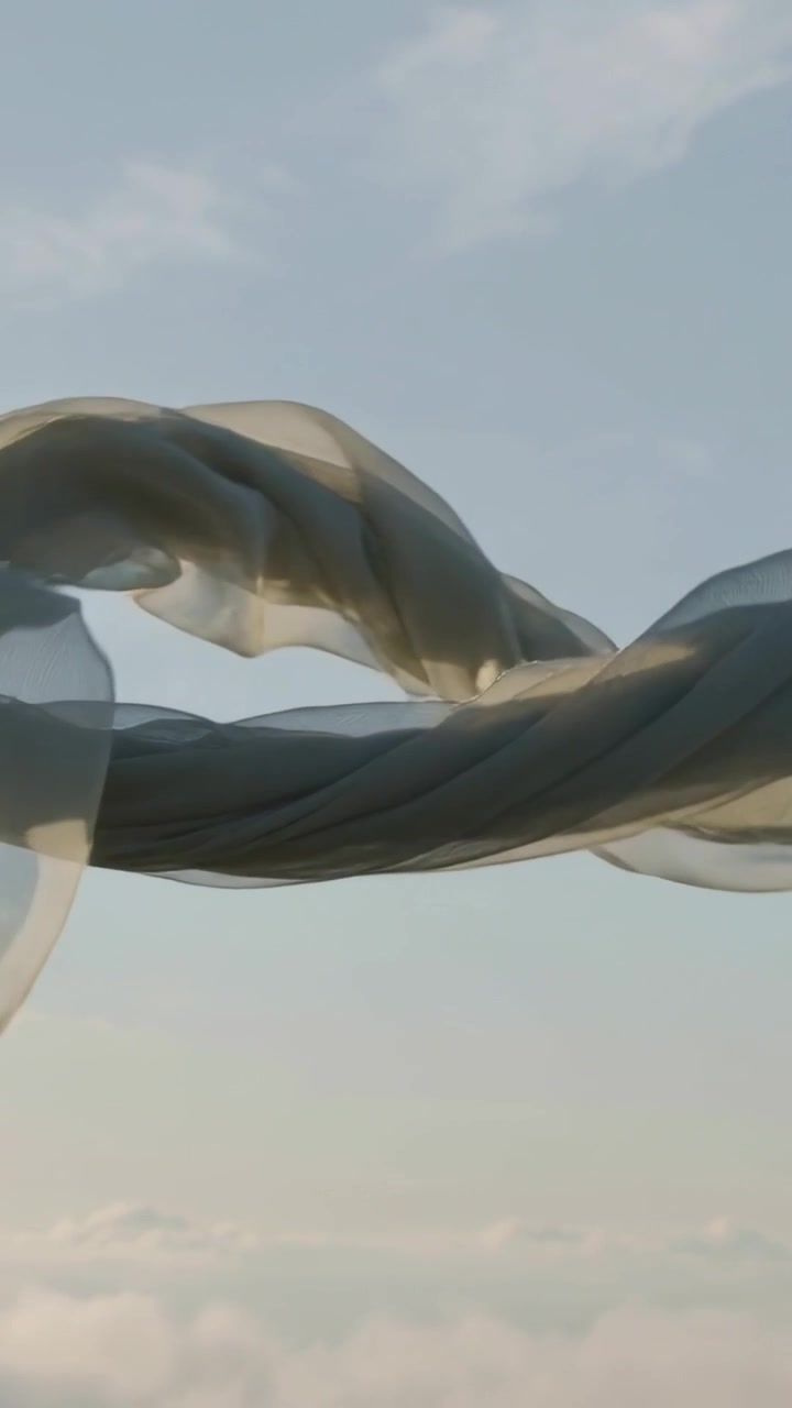 Vertical video: Lifting sheer scarf from top-left, breeze carrying folds over pale sky, frayed hem