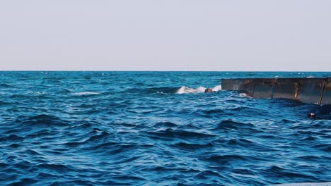 motion of blue ocean water. stone pier in the sea. waves crashing on a stone dock. nice background of blue water. slow motion.