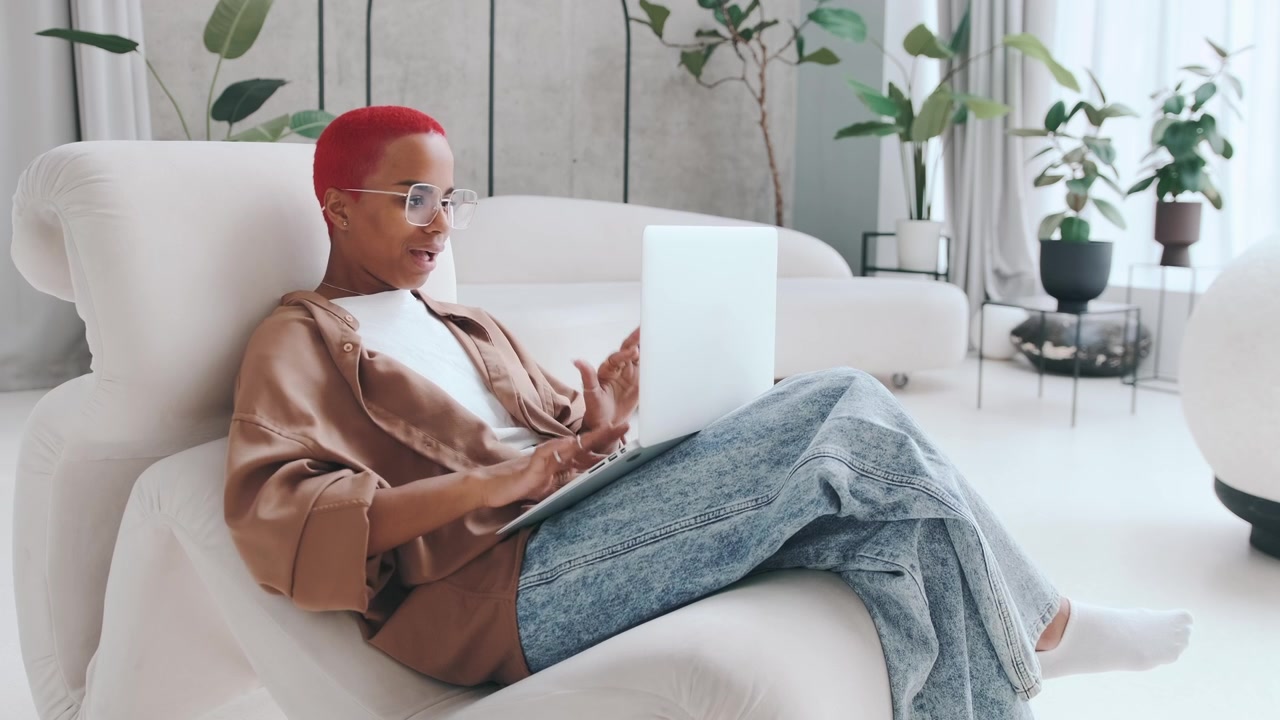 Young african american woman randomly knocking on laptop sits in apartment