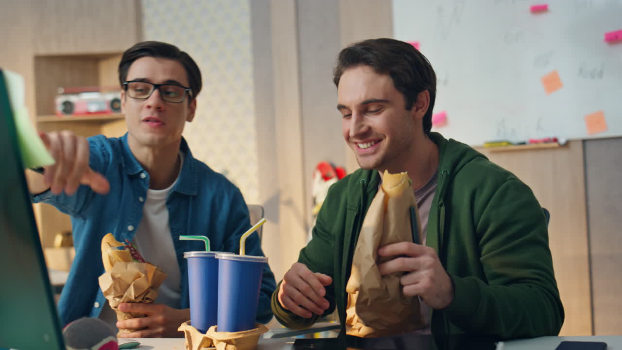 점심을 먹고 있는 사무실 직원들이 모니터를 가까이서 보고 있습니다. 프리랜서 직원들이 몸짓을 하고 있습니다.