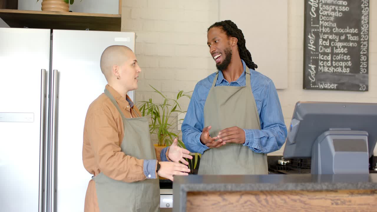 Diverse barista coworkers initiating discussion behind wooden counter to coordinate coffee orders
