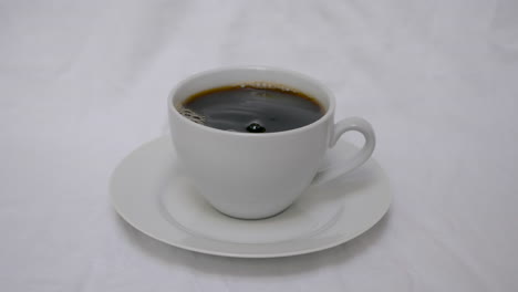 verter azúcar en una taza de café blanca con café en un platillo blanco con fondo blanco