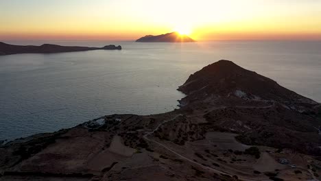 Aerial-sunset-drone-shot-flying-toward-the-sun-setting-on-the-ocean-horizon-and-flying-over-rustic-european-landscape-with-sunburst-over-distant-island