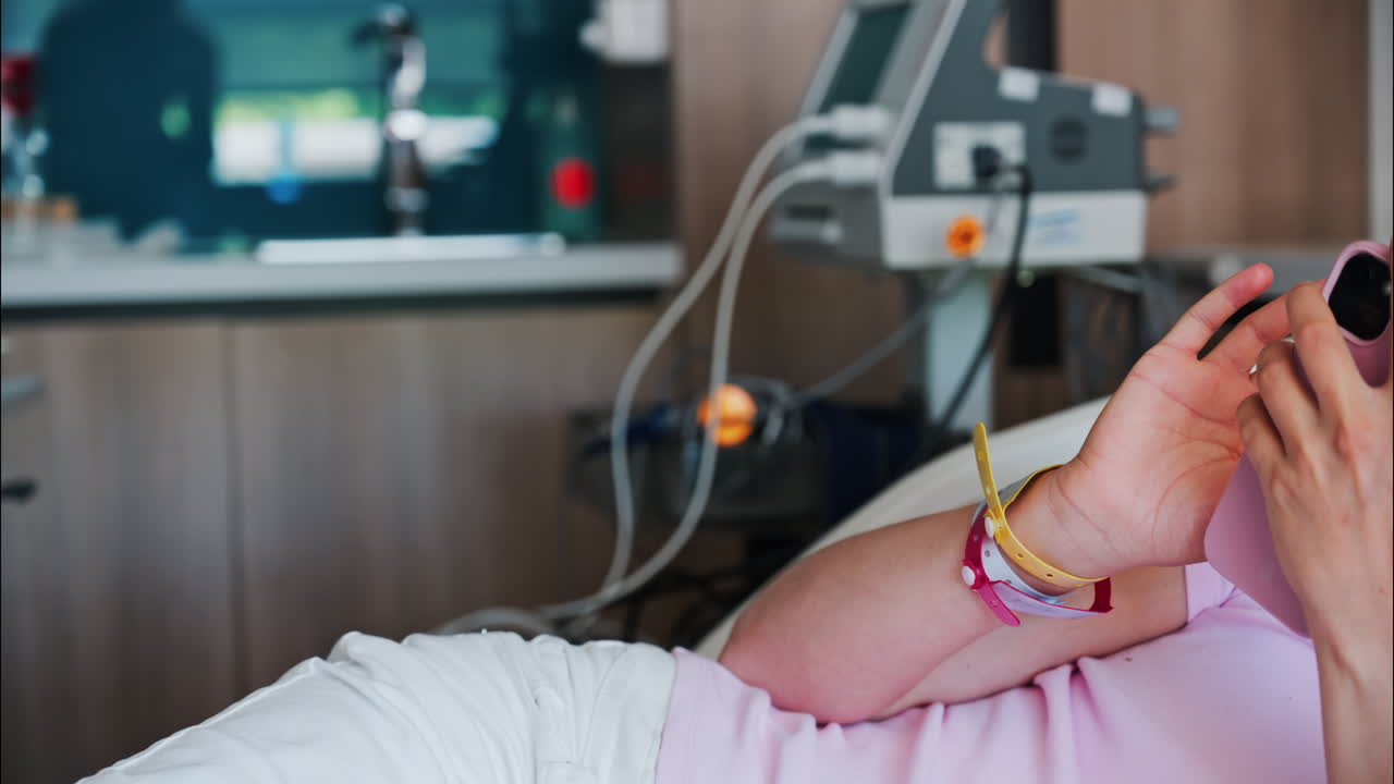 Pregnant woman scrolling on her phone while lying in a hospital bed at the doctor's office