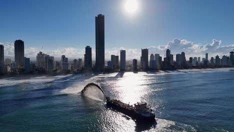 aerial view of a dredging vessel pumping sand near the gold coast skyline during sunset, highlighting urban coastal erosion
