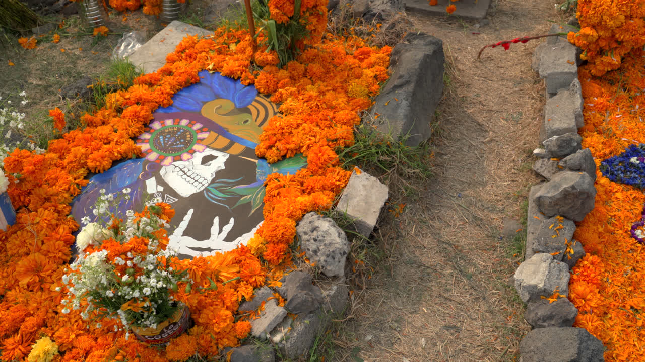 Cempasuchil flowers line a ceremonial pathway with candles and bright offerings for the holiday, establishing pan right