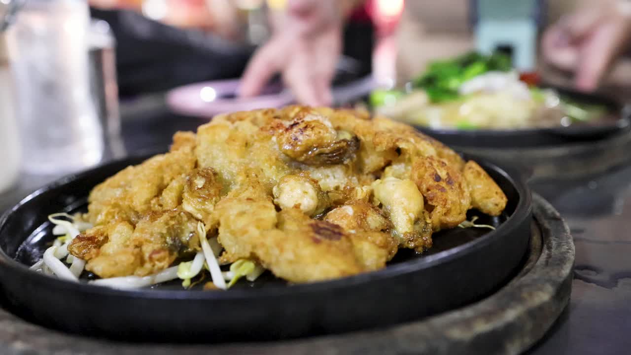 Golden fried oyster pancake on sizzling pan, street food setting, shallow focus, natural lighting