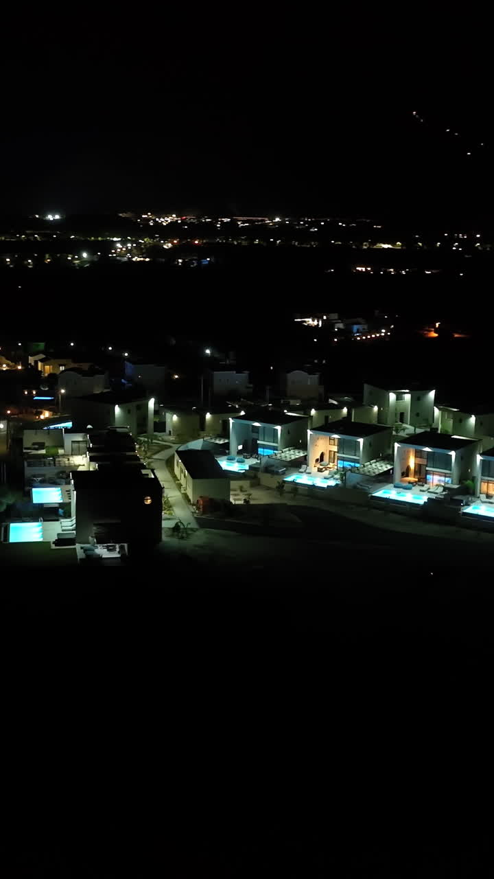 Vertical drone shot circling upscale hilltop, holiiday villas, night in Greece