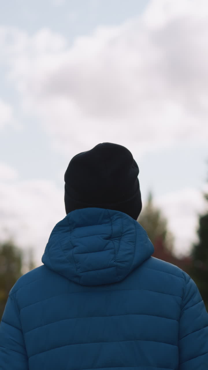 푸른 재과 검은색 베니를 입은 사람이 주거 지역에 산책하고, 구름이 많은 하늘 아래 배경에 흐릿한 집과 나무가 있습니다.