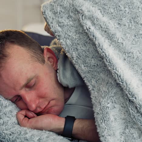 sick man with a headache during fever. guy lying in bed covering his head with a warm blanket. coronavirus pandemic, epidemic. close-up