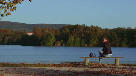 young woman walks up and sits on bench at lake with nice view, static