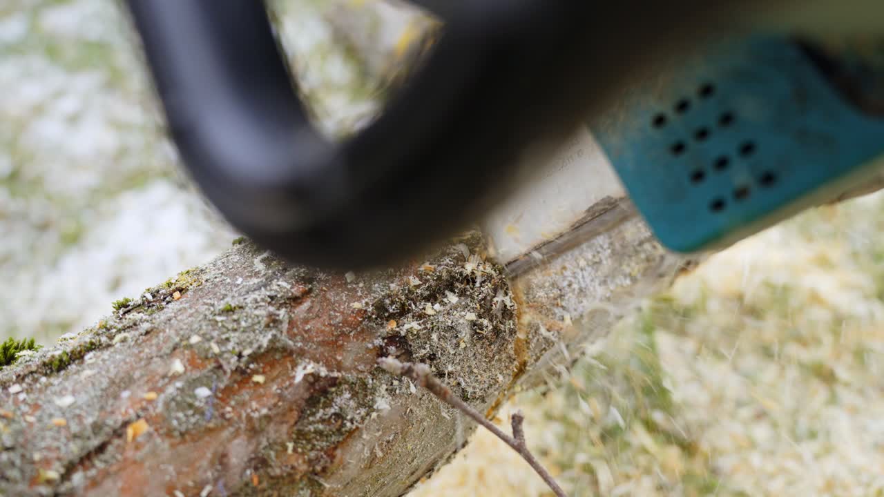 나무 줄기를 자르기 위해 전기 전기톱을 사용하는 사람, 공중에 나무 먼지 날리기