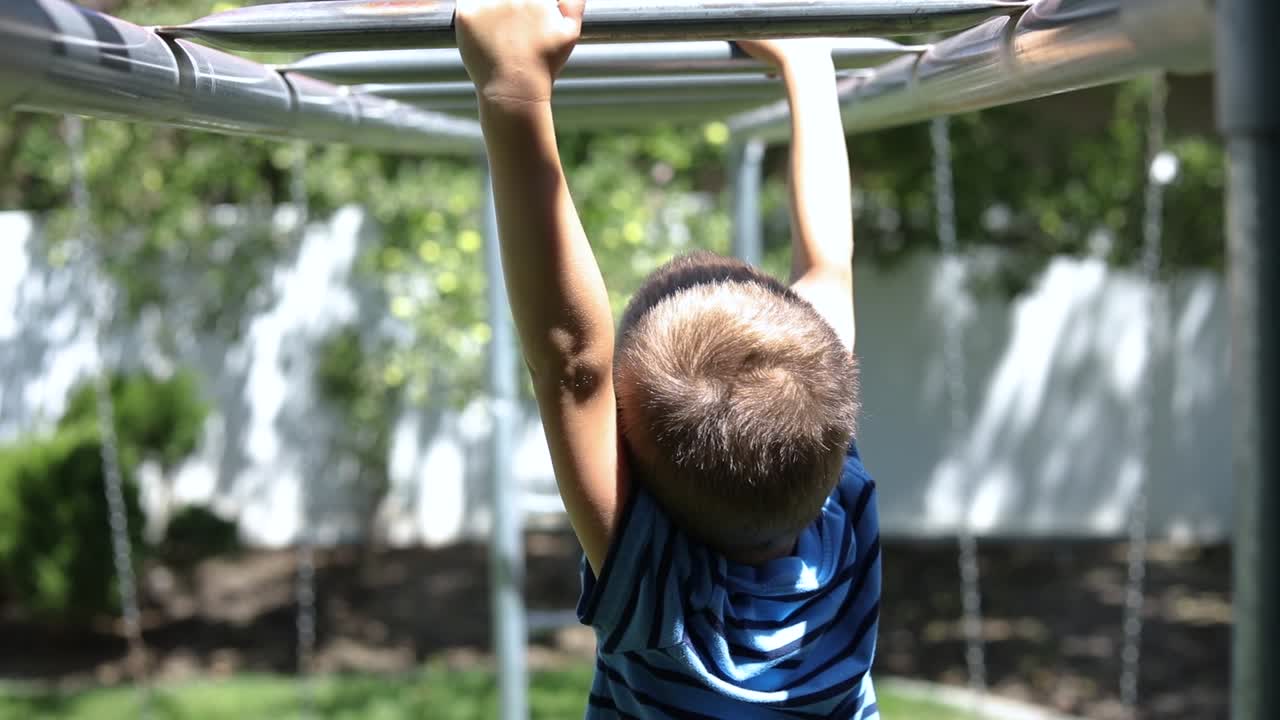 toma en cámara lenta de un niño jugando en las barras de mono en un patio de recreo en su patio trasero