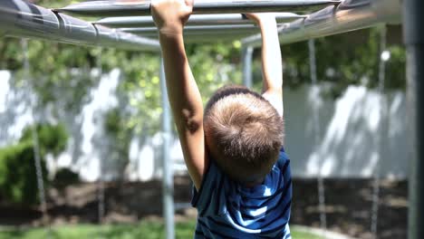 slow motion shot of a young boy playing on the monkey bars on a playground set in his backyard