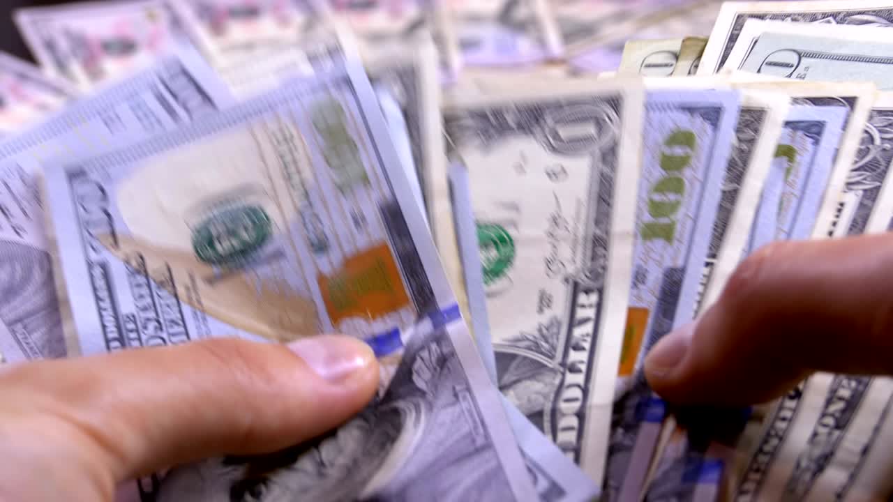 las manos de los hombres sostienen un montón de dólares estadounidenses contra el fondo de dinero giratorio