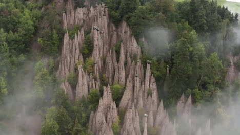 aerial view tilting through fog, revealing the piramidi di terra, in south tyrol, italy