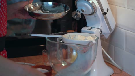 adding flour to ingredients in mixer bowl through a sieve