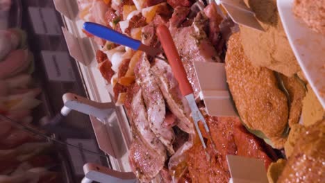 vertical video of a gloved deli worker selects a portion of fresh cut meat from a specialty counter