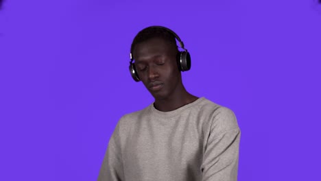 Pleased-african-man-in-white-shirt-and-headphones-dancing-relaxfuly-with-eyes-closed-over-blue-background.-Slow-motion
