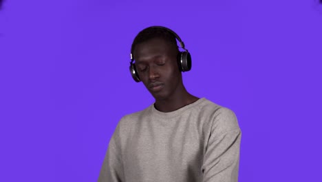 pleased african man in white shirt and headphones dancing relaxfuly with eyes closed over blue background. slow motion