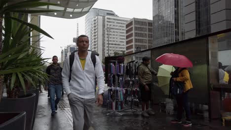 foot traffic increases as people walk along a wet city street, carrying umbrellas to shield themselves from the rain during a bustling afternoon. umbrella street vendor