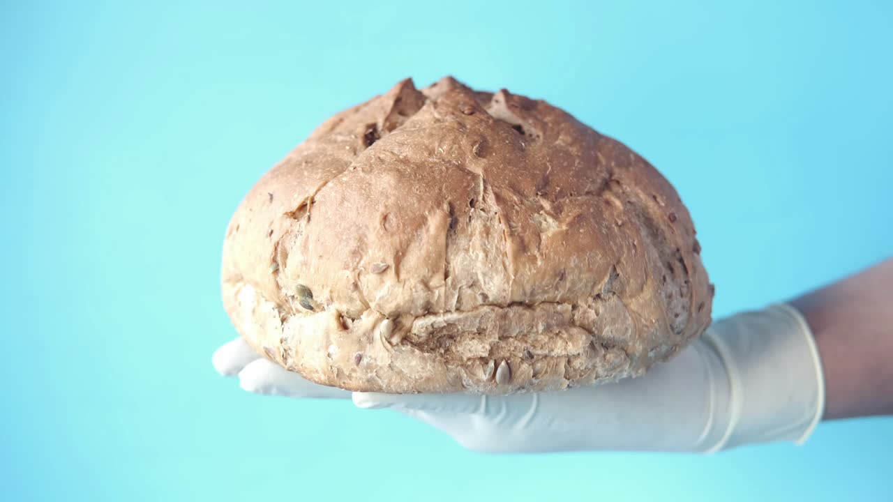 hand in gloves holding round brown baked bread
