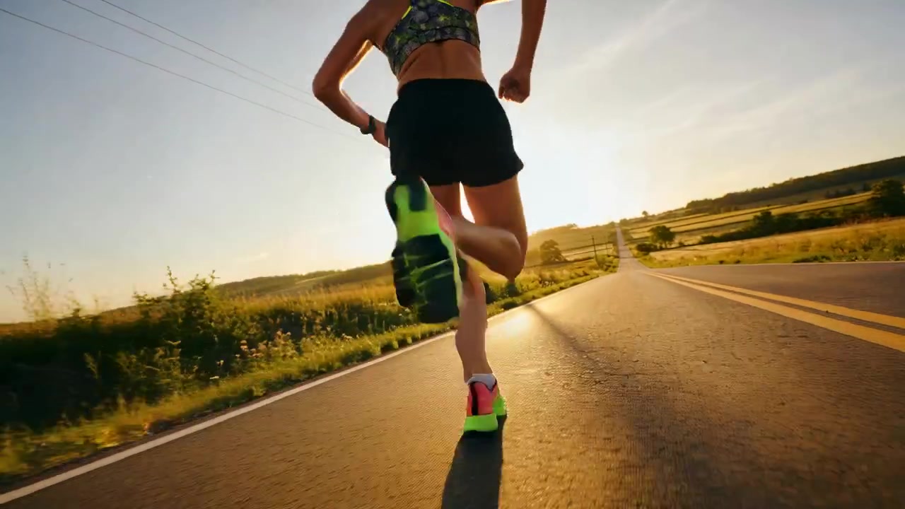 Donna che corre allenandosi con appoggio del tallone lungo una strada rurale a due corsie, indossando scarpe color neon.