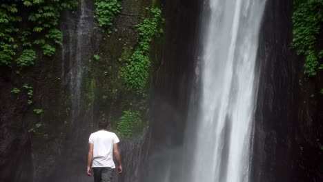 Man walking towards Munduk Waterfall, surrounded by lush greenery, misty and serene