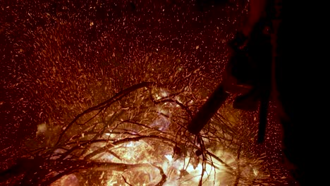 man blowing burning tree branches bonfire and embers with blower at night