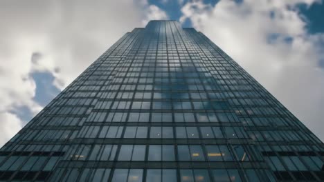 a modern skyscraper reaches for the sky, its reflective glass facade mirroring the clouds and creating a stunning visual display in the bustling cityscape.