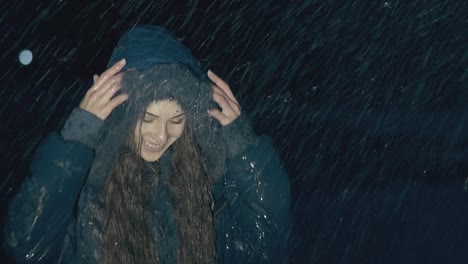 woman with dark hair in jacket jumps for joy in heavy rain