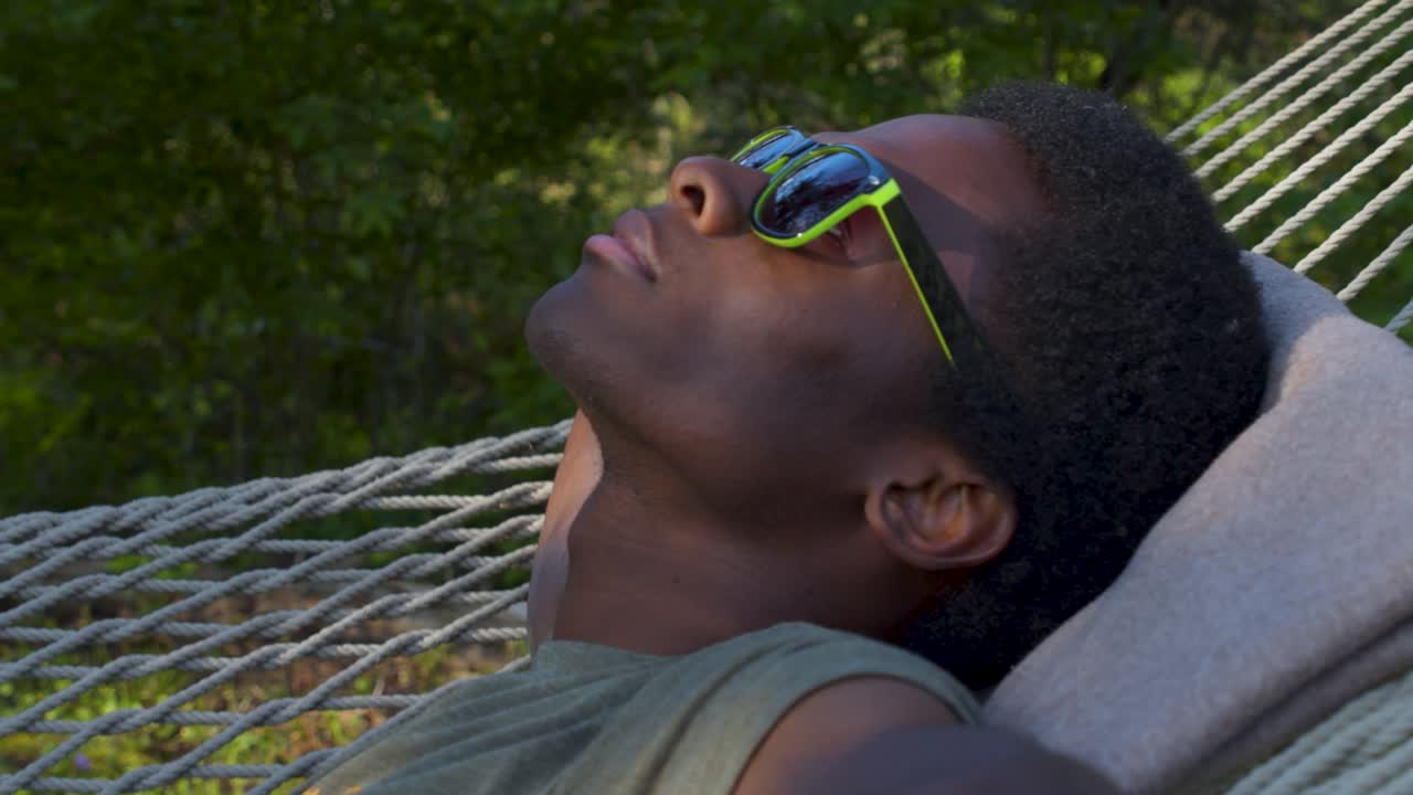 Black Man with sunglasses lying on swinging hammock outdoors, close up