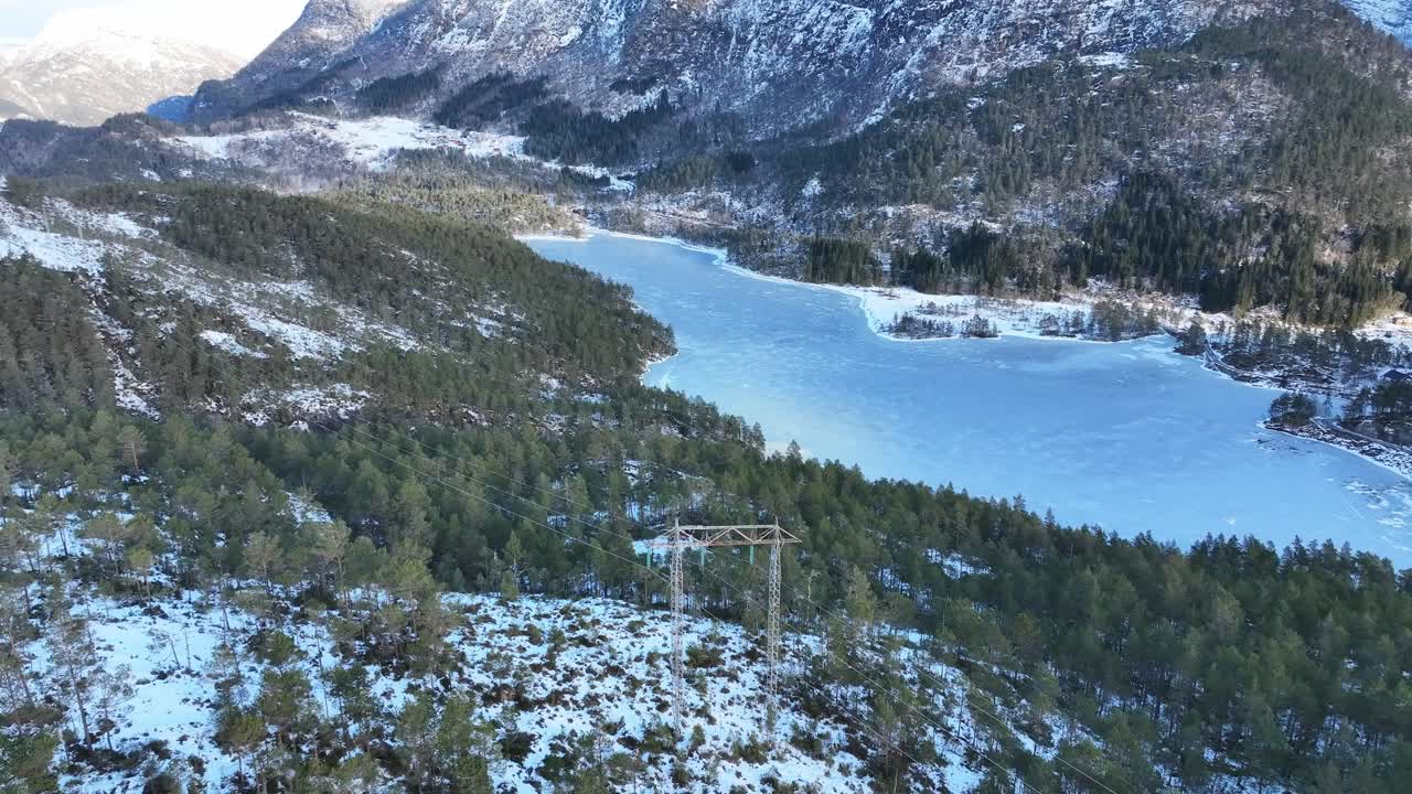 Pohled z výšky obkrouží stožár elektrického vedení a odhaluje zamrzlé jezero a přenosová vedení táhnoucí se zimní krajinou Norska.