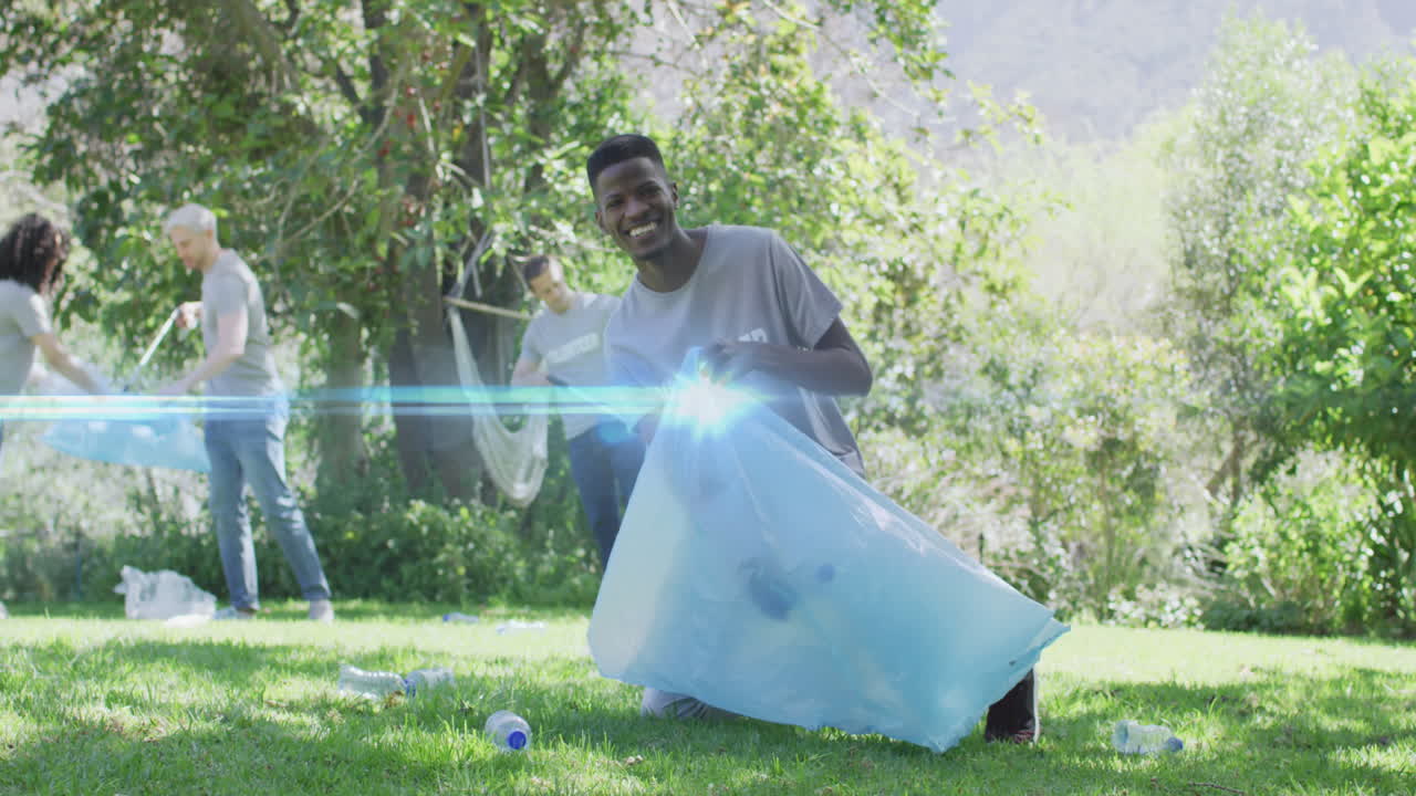 Video of lights over happy diverse group picking up rubbish in countryside