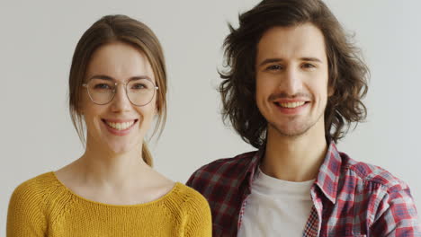 close up of the young couple in love looking at each other and smiling to the camera on the white background wall